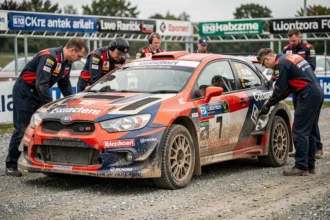 Voiture de rally d'occasion couverte de boue lors d'un événement étranger entourée de mécaniciens